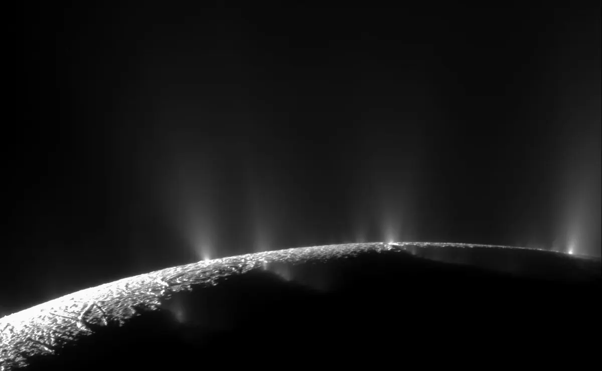 The limb of Enceladus in black and white with many thin jets of ice spraying from the surface into space