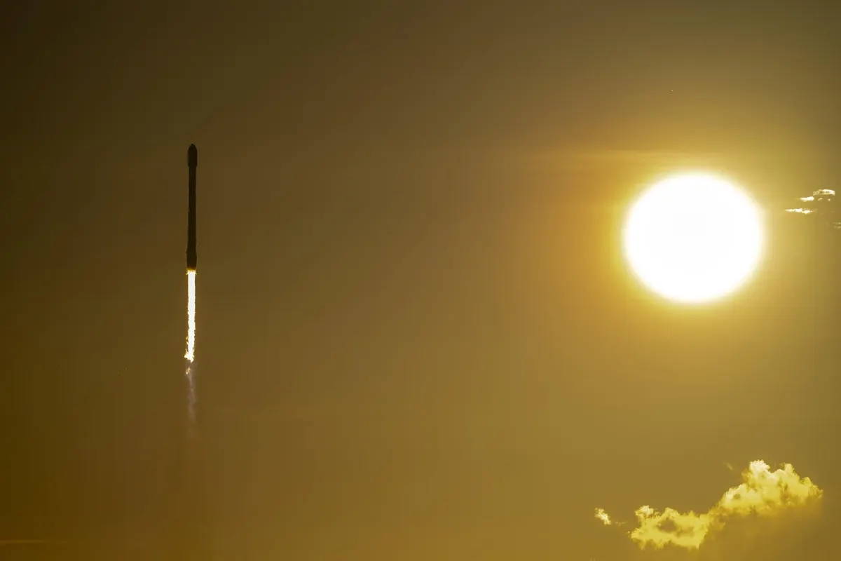 A Falcon 9 rocket climbing past the setting Sun with a long exhaust trail