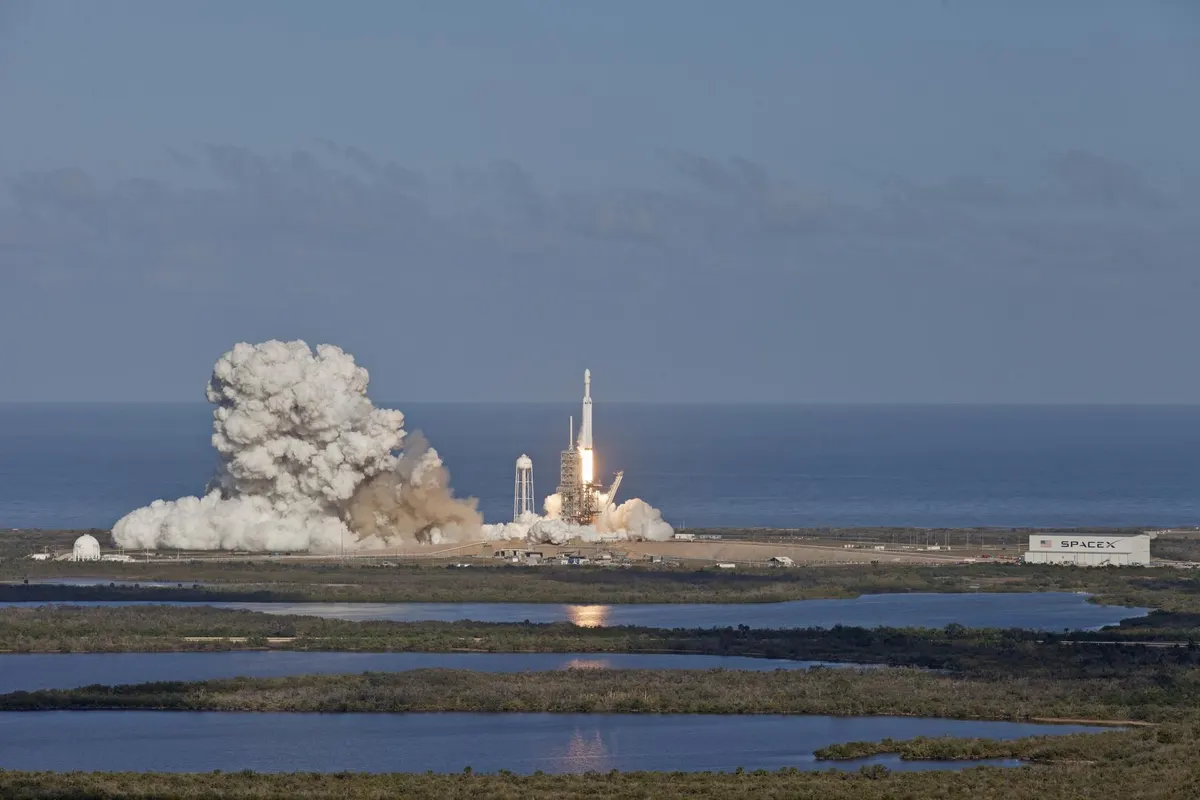 A Falcon Heavy rocket lifting off from a Florida launch pad with a large plume of smoke