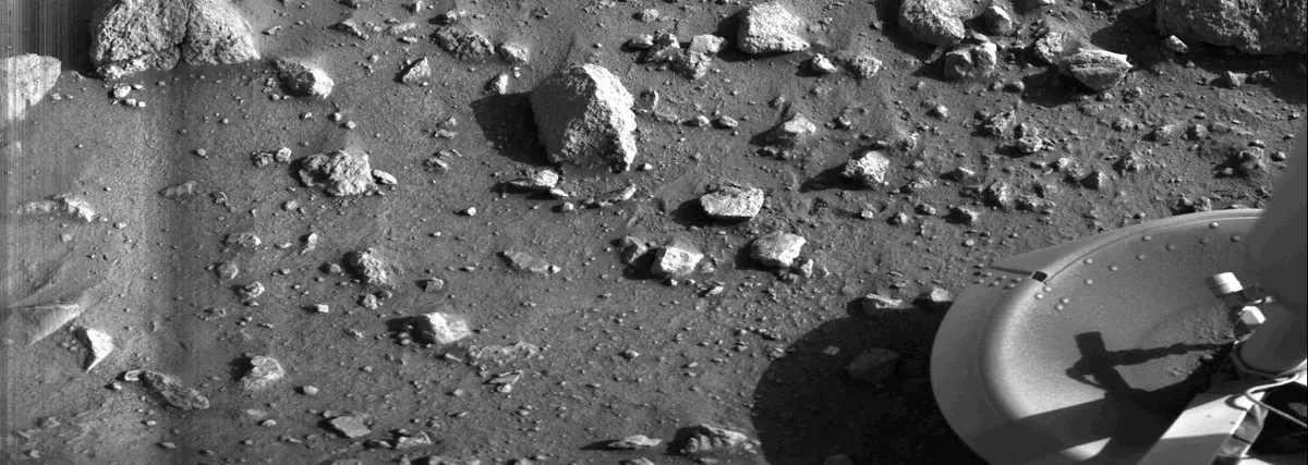 Rocks and fine soil on the surface of Mars with part of a lander at the lower right