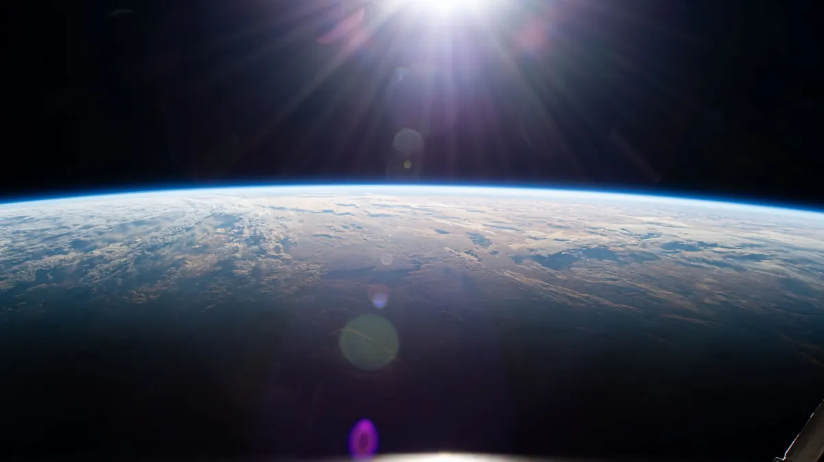 Sunrise over Earth seen from orbit, with a bright glow above a cloudy ocean