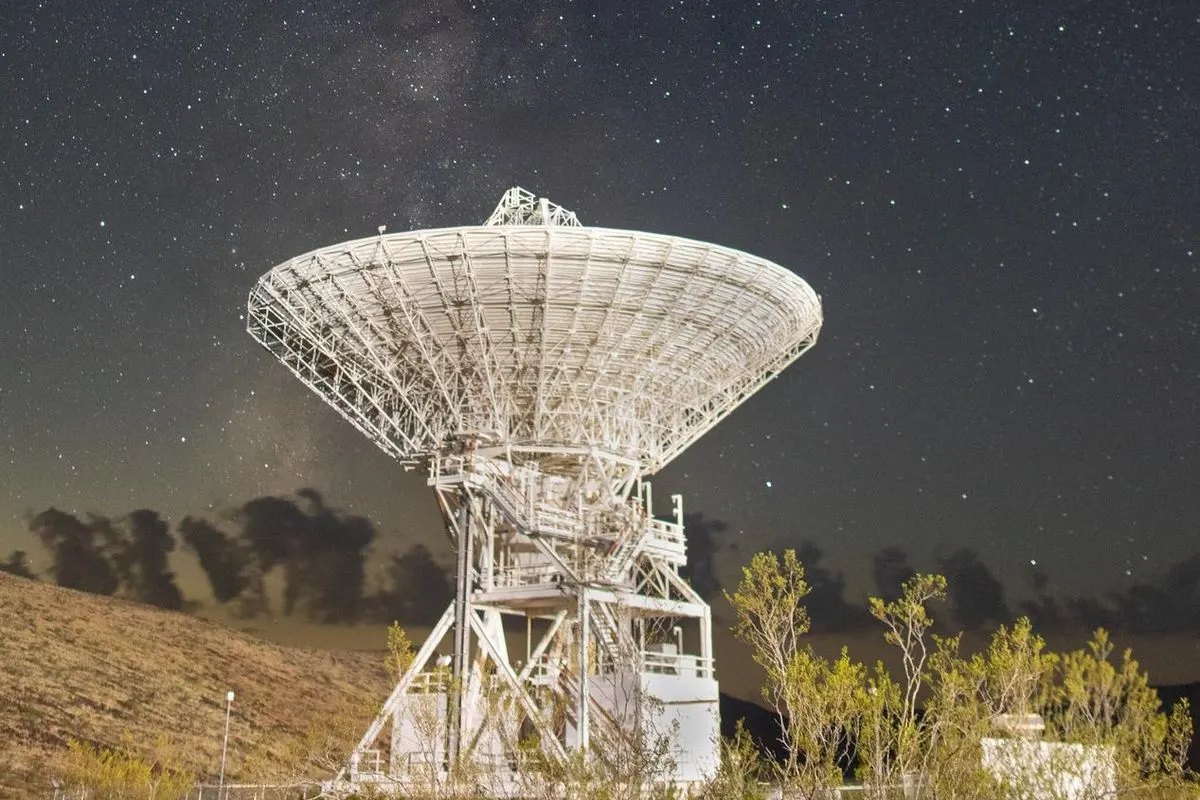 A white radio telescope dish under a starry sky with the Milky Way above it