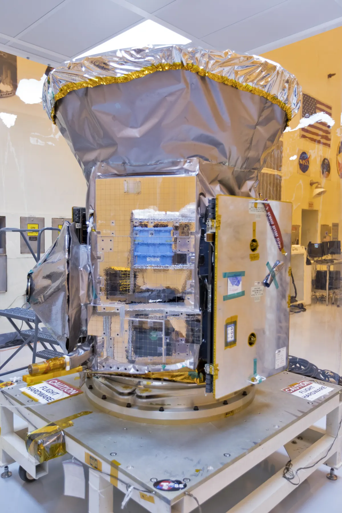 The TESS satellite with its gold-colored insulation inside a clean room, with technicians working around it