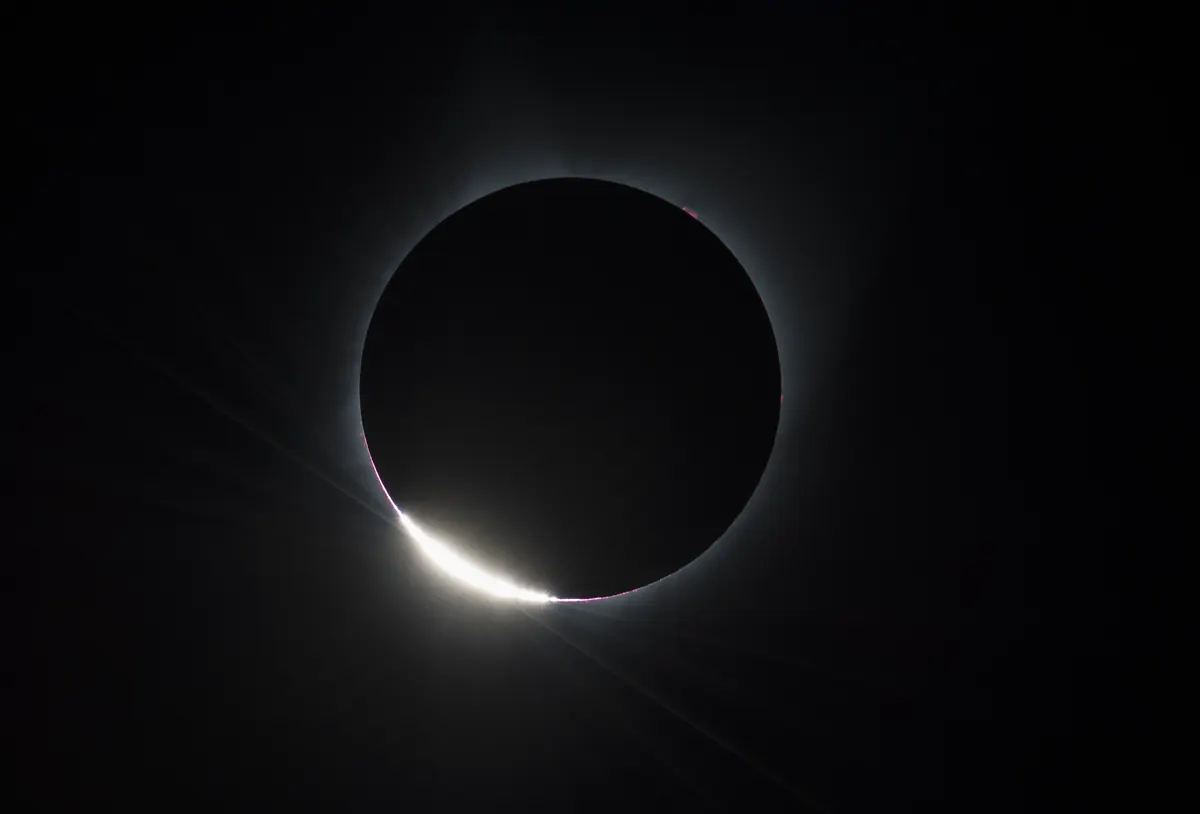 The black disc of the Moon with a bright flash of sunlight at its lower edge, the diamond ring effect