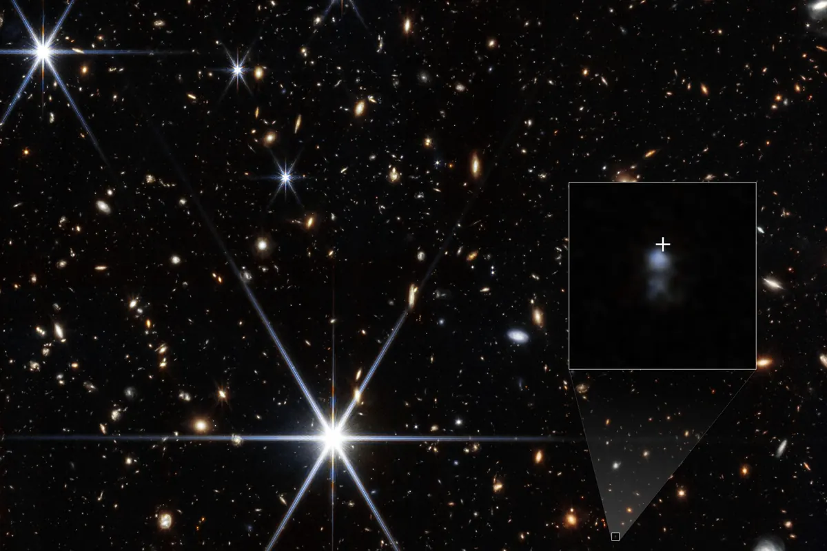 A field of galaxies in near-infrared light, with a small inset zoomed on a faint blue dwarf galaxy marked by a white cross